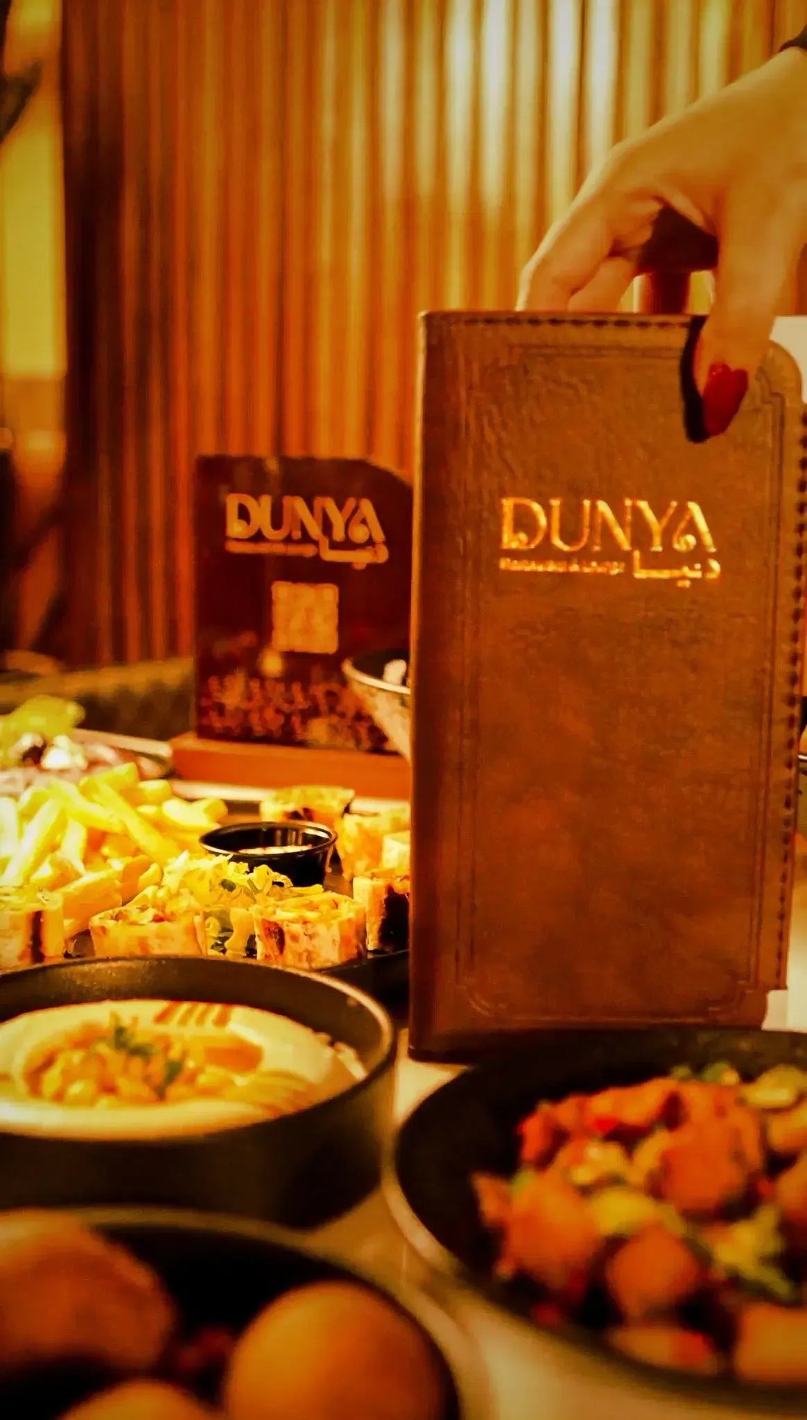 DUNYA menu held over a warm spread of mezze and fries