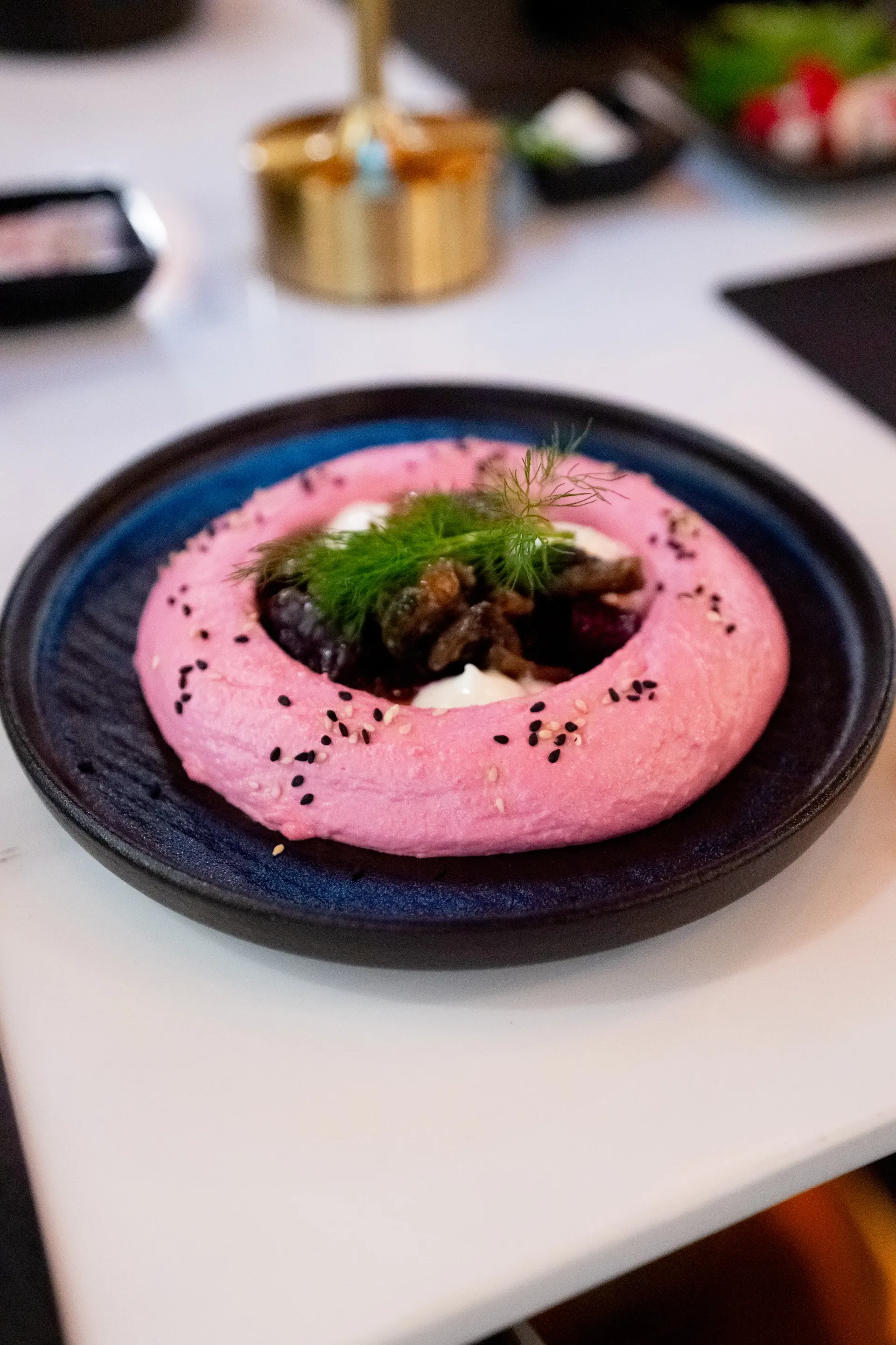 Beetroot hummus on a dark blue plate with fennel and sesame at DUNYA